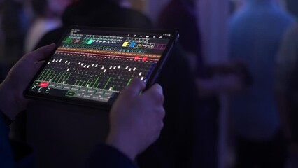 DJ sound control in application on the tablet for mixing instruments of music band in disco club concert hall. Hands touching buttons sliders, levels of volume changing.