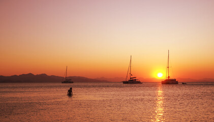 Sailboats cruising in Mediterranean coves and vacationers swimming at sunset