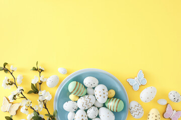 Easter celebration idea. Top view photo of circle plate with colorful easter eggs butterfly cookies and spring blossom flowers on isolated yellow background with empty space