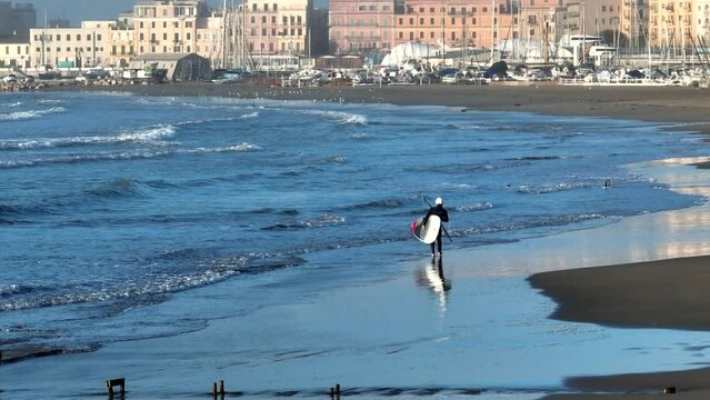 surfista cammina sulla spiaggia con la tavola da surf. Anzio, Roma, Italia.
Ripresa aerea con drone della costa e del porto.