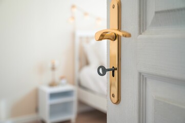 Closeup shot of a white open door with a key in it with a bedroom in a blurry background.