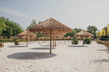 Fototapeta na wymiar Sunny sandy beach with straw tiki umbrellas