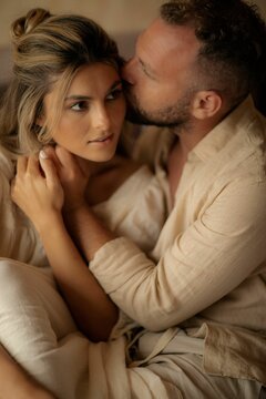 an attractive young couple hugging in bed while the man kiss his wife's forehead