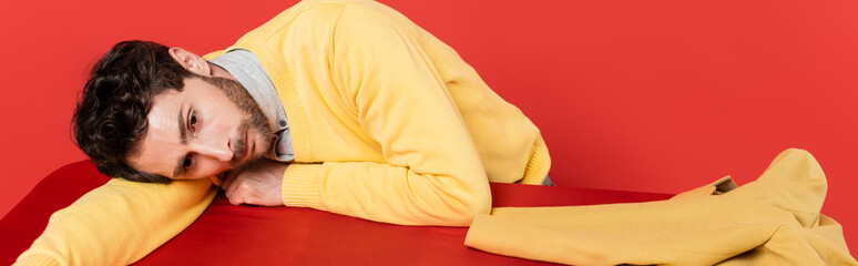 tired guy in yellow long sleeve jumper lying on red desk near blazer isolated on coral background, banner.