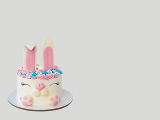 White and pink cake with cute bunny for children's birthday or Easter. Bunny made of fondant and buttercream. Grey background. Horizontal orientation