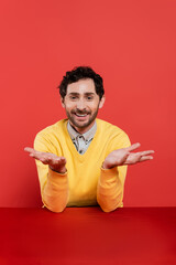 carefree man in yellow long sleeve jumper gesturing on red coral background.
