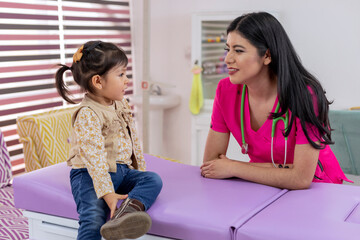 A young female pediatrician talking with a little girl in her medical office