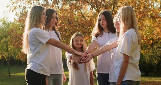 Group of teenage girls put palms of hands together demonstrating strong unity and friendship in yellowed park. Teenagers enjoy friendship