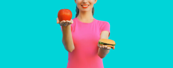 Fast food and healthy nutrition, happy smiling woman making choice showing apple or burger on blue...