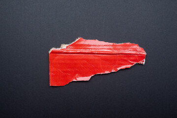 Recycled red cardboard piece. Torn paper on a black background.