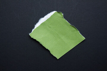 Green torn paper piece isolated on a black background.