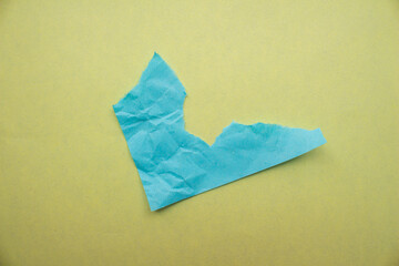 Creased blue paper piece on a yellow background. Crumpled torn paper edge texture background.
