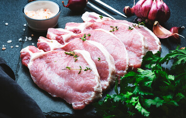 Raw pork chops on black slate board prepared for cooking with garlic, thyme, spices and pepper....