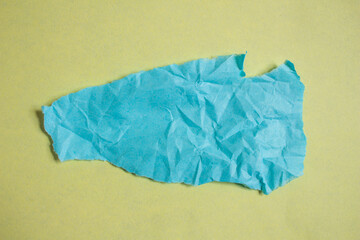 Creased blue paper piece on a yellow background. Crumpled torn paper edge texture background.