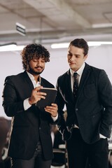 Curious businessmen watching video on tablet. Indoor shot of coworkers in black suits using digital gadget in office