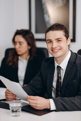 Smiling young businessman holding document. Indoor shot of happy manager doing paperwork in office....