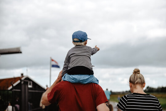 Un niño pequeño señala al frente mientras es llevado a hombros por su padre. Concepto de viajar con hijos.