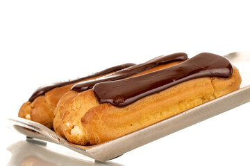 Three sweet chocolate eclairs on a metal plate, close-up, isolated on white background.