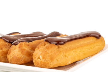 Several sweet chocolate eclairs on a white ceramic dish, close-up, isolated on a white background.