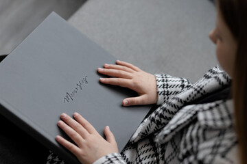 Photo of a gray leather photo book with the inscription memories in the hands of a 10-year-old...