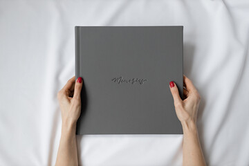 Close-up of a gray leather photo book with memories embossed in the hands of a girl with a red...