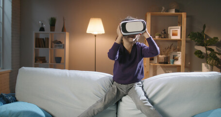 Diving into World of Virtual Reality. Funny little Asian boy with curly hair at home alone trying...