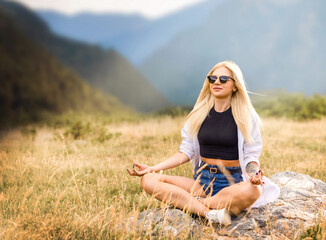 a pretty young woman, blonde, is meditating in nature, enjoying the views in the mountains, harmonia concept with herself, meditation, tourism, weekend, healthy life style
