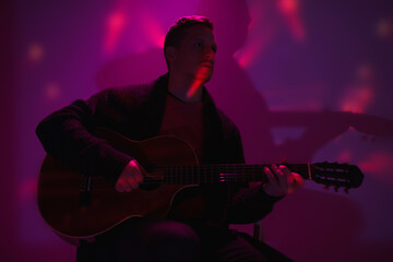 Musician playing acoustic guitar in a foggy club with colorful lights.