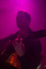 Musician playing acoustic guitar in a foggy club with colorful lights.