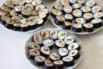 Plates with homemade sushi rolls on white table. Tuna and vegetable sushi, and vegetarian cream cheese and vegetable sushi. Selective focus.