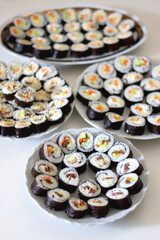 Plates with homemade sushi rolls on white table. Tuna and vegetable sushi, and vegetarian cream cheese and vegetable sushi. Selective focus.