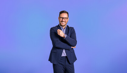 Portrait of confident young adult handsome CEO dressed in blue suit wearing eyeglasses and posing cheerfully against blue background