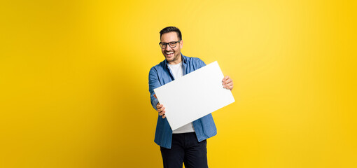 Cheerful male professional showing white blank banner for business advertising and looking at...