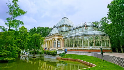 Fototapeta na wymiar Palacio de Cristal del Retiro, Madrid, Spain - May 28, 2018: Crystal Palace with glass structure surrounded by trees and pond in Buen Retiro Park