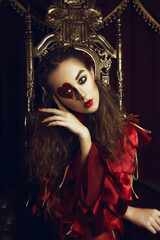 Woman dressed as the queen of hearts, creative make up with big heart on eye, girl sitting in the throne, hi-end retouched portrait