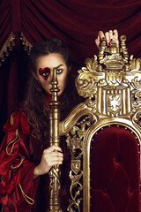 Woman dressed as the queen of hearts, creative make up with big heart on eye, girl sitting in the throne, hi-end retouched portrait