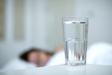 Young woman in the bed in bedroom at home in the morning lying under white blanket and drinking pure fresh water from glass 
