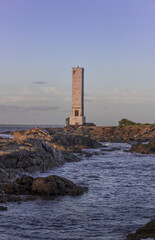 lighthouse on the coast at sunset sunlight and waves rocks on beach
