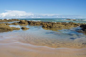 beach and rocks and the sea with waves transparent water clouds on the sky