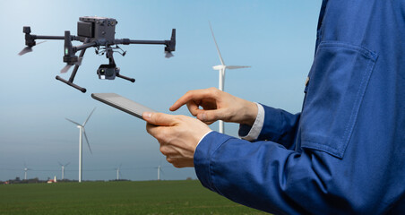 Engineer with tablet computer controls drone on a background of wind turbines	