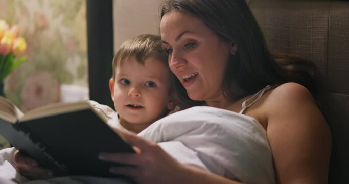 Mother reading a fairytale to her lovely small son in bed before going to sleep