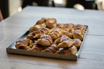 bandeja de metal aluminio con muchas medialunas de manteca en bar cafetería panadería restaurante sobre mesa de madera ventana ventanal
