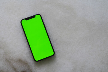 A top view of smartphone with green screen template for social media, web or app mock up. Marble background