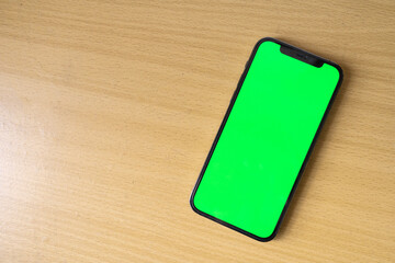 A top view of smartphone with green screen template for social media, web or app mock up. Pine wood background