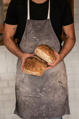 hombre con delantal sosteniendo dos panes de masa madre con delantal en restaurante panadería