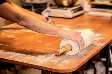 producción panadería hombre trabajando enrollando masa de harina sobre mesa de madera con palo de...