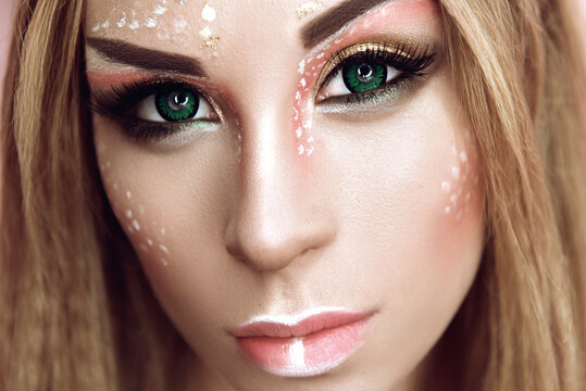 Young attractive cute girl with an unusual creative make-up of wild deer. Halloween ideas of beauty photography