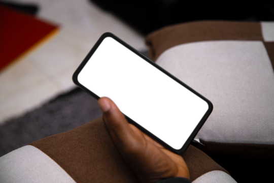 Black Hand holding mobile phone with transparent blank png screen in living room