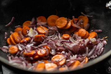 Onions and carrots are fried in a deep frying pan. Preparation for cooking.