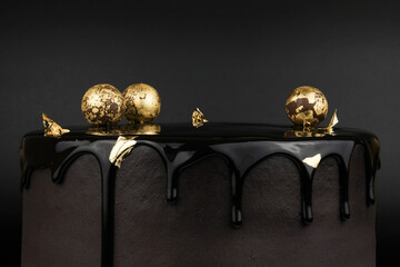 Chocolate cake with black glaze, decorated with balls in gold on a black background.